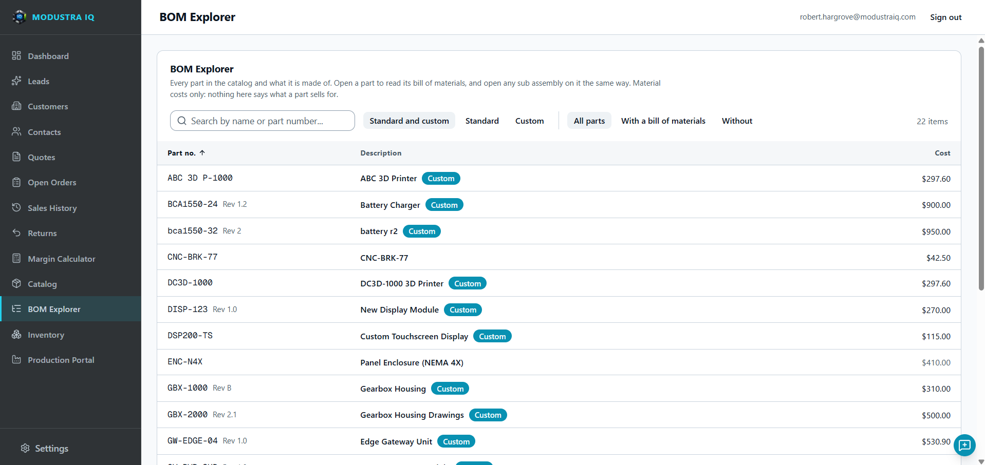 The Modustra IQ BOM Explorer: a search box, filters for standard and custom parts and for parts with or without a bill of materials, and a list of catalog parts with part number, revision, description, a Custom badge where it applies, and material cost.